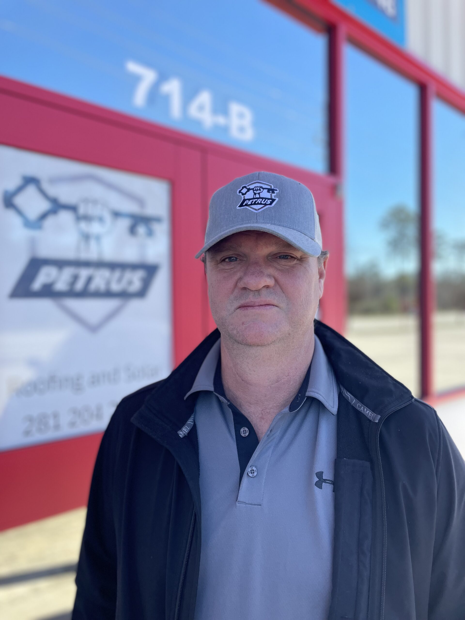 John with hat and coat stands in front of the Petrus office front doors.